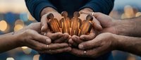 Close-up of two male hands holding golden ammunition cartridges together outdoors with blurred urban background, symbolizing unity and shared responsibility.