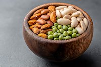 Mixed nuts and legumes in wooden bowl on dark background, including almonds, pistachios, green peas and cashews, healthy protein snack food.