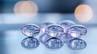 Transparent glass beads with pink and blue reflections arranged in row on reflective surface create ethereal macro composition with bokeh background effect.