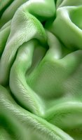 Soft waves of light green velvet fabric create flowing curves and gentle folds with delicate texture and subtle shadows, suitable for luxury fashion and interior design backgrounds.