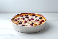Fresh baked cherry clafoutis in white ceramic baking dish on marble surface, traditional French dessert with powdered sugar and whole cherries.