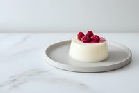Fresh raspberries garnish creamy panna cotta dessert on minimalist gray plate against marble surface, elegant food photography composition.