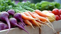 Fresh organic vegetables including purple turnips, orange carrots, and leafy greens arranged at farmers market for healthy cooking and nutrition.