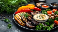 Grilled vegetables platter with hummus dip, fresh herbs, and colorful bell peppers served on dark plate. Mediterranean appetizer with mushrooms and broccoli.