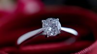Elegant solitaire engagement ring with round brilliant cut diamond in white gold setting against deep red velvet background, macro jewelry photography.