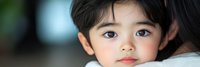 Young Asian toddler girl with dark hair and brown eyes looking directly at camera with innocent expression in soft natural lighting for family content.