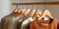 Neutral earth tone clothing on wooden hangers in minimalist closet, showcasing sustainable fashion essentials for capsule wardrobe styling.