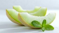 Fresh honeydew melon slices with bright green flesh and mint leaf garnish on white background, showcasing juicy texture for food photography.