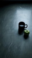 Black mug with water and green apple on dark textured surface, minimalist still life composition for beverage, health, wellness and lifestyle design projects.