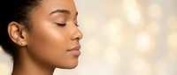 Young African American woman with closed eyes in peaceful meditation pose against soft golden bokeh background for wellness and mindfulness concepts.