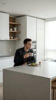 Young professional businessman drinking coffee in modern white kitchen with minimalist design and natural lighting during morning routine.