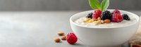 Creamy yogurt bowl topped with fresh raspberries, blackberries, nuts and mint leaves on white marble surface for healthy breakfast concept.