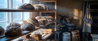 Artisan bread loaves displayed on wooden shelves in a bakery window with warm natural light, showcasing freshly baked goods for retail sale and bakery business promotion.