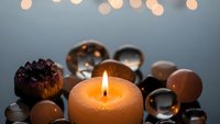Burning candle surrounded by decorative glass spheres and natural elements creating warm ambient lighting for relaxation and meditation practices.