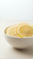 Fresh lemon slices arranged in white ceramic bowl on neutral background for culinary and wellness content.
