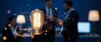 Glowing vintage filament bulb with golden light trails and sparks, symbolizing innovation and creative ideas in modern business environment with blurred professionals.