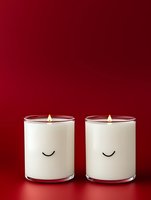 Two white minimalist candles with cute sleeping faces and warm flames on deep red background for cozy home decor and relaxation atmosphere.