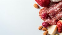 Gourmet food composition with sliced salami, cheese, fresh strawberries, raspberries and almonds on white background with copy space.