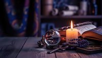 Mystical fortune telling setup with crystal ball, burning candle, tarot cards and ancient books on wooden table for divination and spiritual guidance.