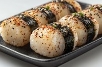 Japanese rice balls onigiri with nori seaweed strips and sesame seeds served on black ceramic plate, close up view of traditional Asian cuisine appetizer.