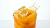 Fresh tropical fruit juice splashing in glass with ice cube and star fruit slice, vibrant orange drink on white background.