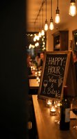 Cozy restaurant interior with happy hour chalkboard sign advertising wine and bites, warm pendant lighting creates inviting atmosphere for dining and socializing.