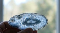 Blue agate geode slice with crystalline formations held in hand against blurred natural background for geology education and mineral collection display.