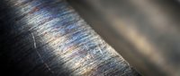 Macro close-up of brushed metal surface with rainbow iridescent reflections and scratched texture for industrial design backgrounds.