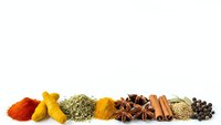 Colorful spices and herbs arranged in a row on white background including turmeric, paprika, cinnamon, star anise and peppercorns for cooking.