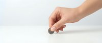 Hand holding single coin above white surface showing financial concept for savings investment and money management decisions.
