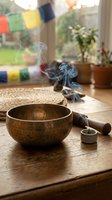 Tibetan singing bowl with incense smoke on wooden table near window with prayer flags for meditation and spiritual wellness practices.