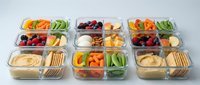 Healthy meal prep containers with fresh vegetables, fruits, crackers and dips arranged for weekly planning and nutritious eating habits.