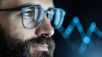 Middle Eastern man with beard and glasses in profile view against dark background with blue bokeh lights creating modern tech atmosphere for business concepts.