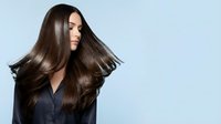 Young Asian woman with long flowing brown hair in motion wearing black shirt on light blue background for beauty and haircare advertising.