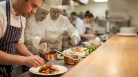 Professional chefs plating gourmet dishes in commercial kitchen restaurant. Culinary team preparing fine dining meals with precision and teamwork.