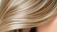 Flowing blonde hair with natural highlights and lowlights creates soft waves and movement against neutral background, showcasing professional hair coloring and styling techniques.