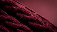 Burgundy cable knit wool sweater texture with intricate braided pattern details for cozy winter fashion and textile design projects.