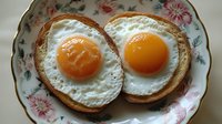 Two perfectly fried sunny-side up eggs with golden yolks on toasted bread slices, served on vintage floral china plate for breakfast meal concept.