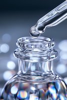 Crystal glass dropper bottle with liquid drop falling into elegant container against blurred bokeh background, macro photography in cool tones.