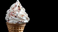 Soft serve vanilla ice cream in waffle cone sprinkled with chocolate shavings against black background, dramatic lighting creates appetizing dessert photography.