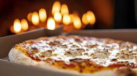 Fresh baked pizza with melted cheese and toppings on dark background with glowing candles creating romantic atmosphere for dining experience.