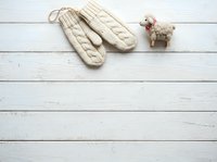 Pair of cream knitted mittens with cable pattern and small decorative sheep figurine on white wooden surface, suitable for winter fashion and holiday design projects.