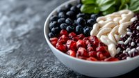 Fresh berries, cashews and black beans arranged in sections in white ceramic bowl on dark stone background. Healthy ingredients for nutritious meal prep.