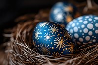 Decorative blue Easter eggs with golden star pattern nestled in natural straw nest, close-up view showing intricate festive holiday details and traditional design.