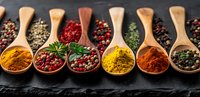 Colorful spices and seasonings in wooden spoons on dark stone background, aromatic curry, paprika, turmeric powder and peppercorns for cooking.
