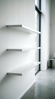 Modern minimalist floating shelves on white wall near window with natural light creating clean geometric shadows for contemporary interior design.