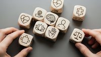 Hands arranging wooden cubes with healthcare and wellness symbols including heart, brain, lotus, medical cross and scales on gray background.