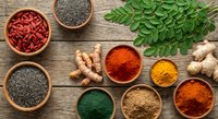 Colorful spices and herbs arranged in wooden bowls on rustic table. Fresh ginger root, turmeric, paprika, chia seeds, goji berries create vibrant cooking ingredients display.