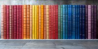 Colorful rainbow arrangement of vintage hardcover books on gray shelf, spines creating gradient pattern from pink through yellow, red, and blue to purple. Library collection.