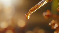 Golden drop of essential oil falling from glass dropper on blurred warm bokeh background, aromatherapy and natural skincare concept for wellness spa.